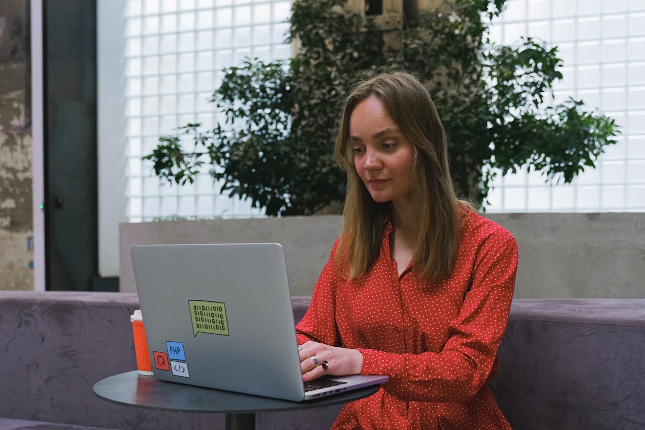 Young woman in red dress using laptop indoors, showcasing remote work lifestyle.